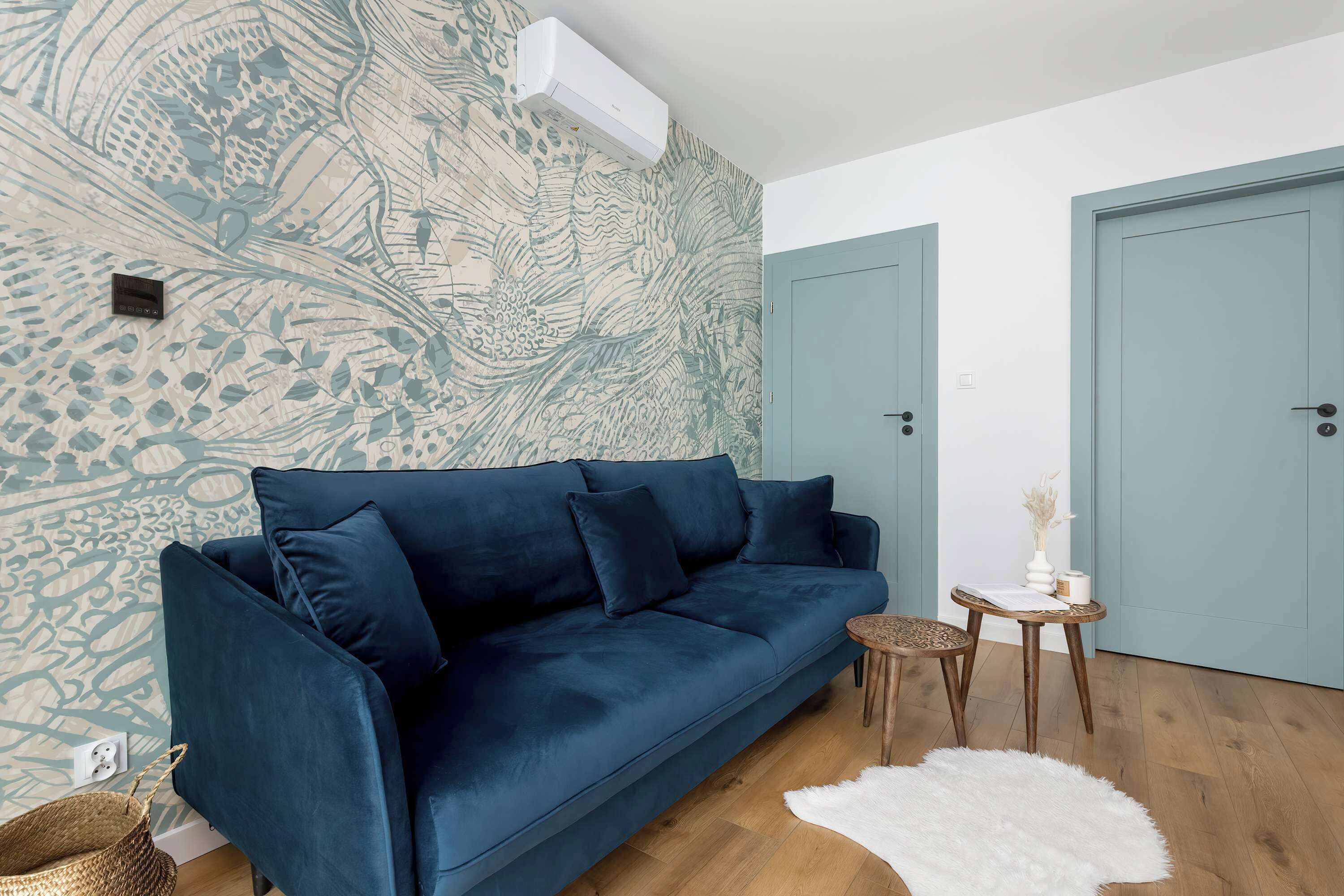 Una sala de estar moderna con un sofá azul oscuro, un muro estampado, una mesita de madera y un tapete mullido blanco.
