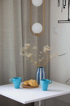 Una mesa blanca con dos tazas azules y un florero azul y blanco a rayas con flores secas.