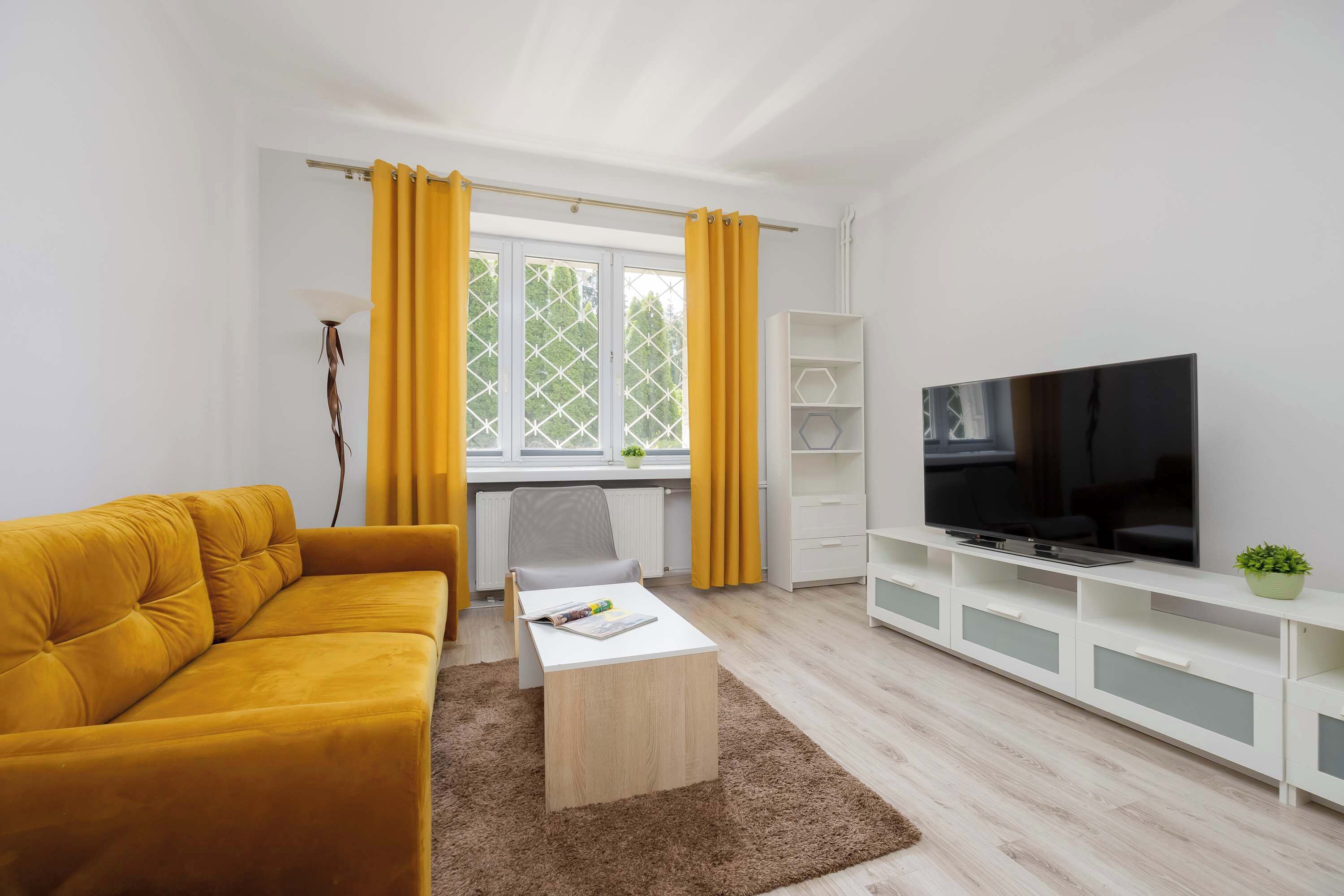 A modern living room with a sofa, coffee table, TV, and a window with curtains.