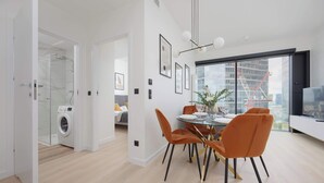 A modern living room with a dining area, a washing machine, and a large window with a city view.