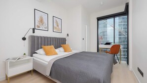 A modern bedroom with a large bed, a bedside table, a chair, and a view of a building through a large window.