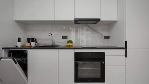 A modern kitchen with white cabinetry, a black oven, and a coffee maker.