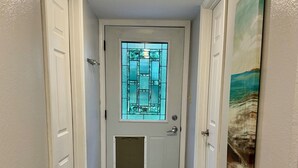 A hallway with a white door featuring a stained glass window, a white rug, and a painting on the wall.