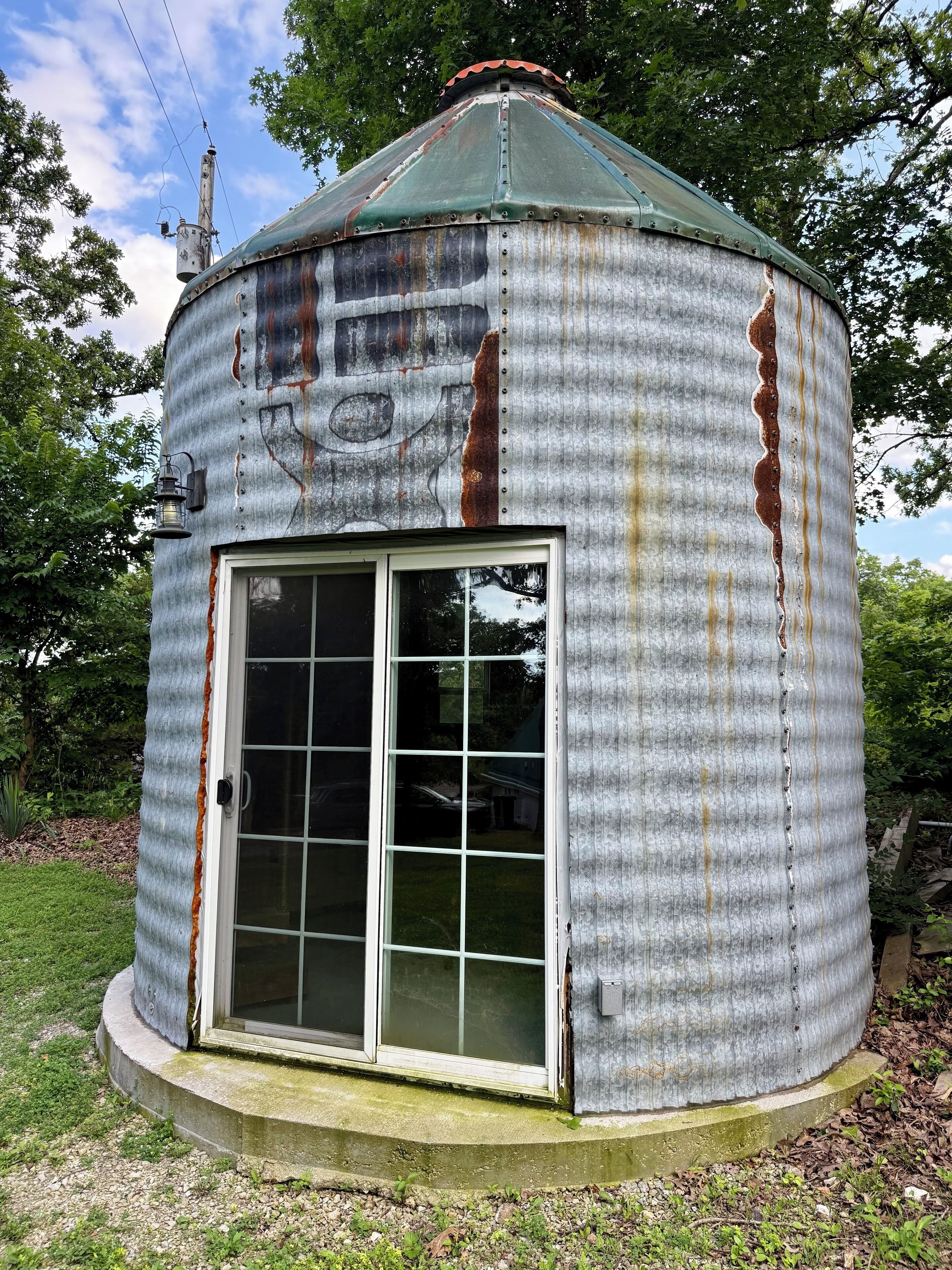 Una estructura metálica cilíndrica con techo verde, puerta de cristal y una pequeña ventana.