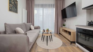 A modern living room with a sofa, a small round table, a TV, and a kitchen area with an oven.