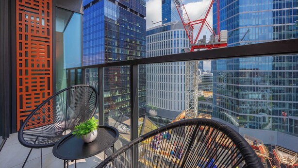 A balcony with two black chairs, a small table with a potted plant, and a view of modern buildings and a construction crane.