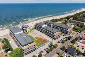 A coastal hotel with multiple buildings, a beach, and a parking area.