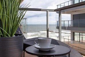 Un balcon donnant sur l’océan, une plante en pot et une table avec une tasse et une soucoupe.