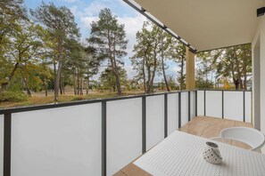 A balcony with a table, chairs, and a view of trees.