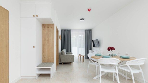 A modern, minimalist room with a sofa, dining table, and chairs, a small side table, and a TV. - Cozy Apartment close to the beach | Parking in the garage (Dąbki)