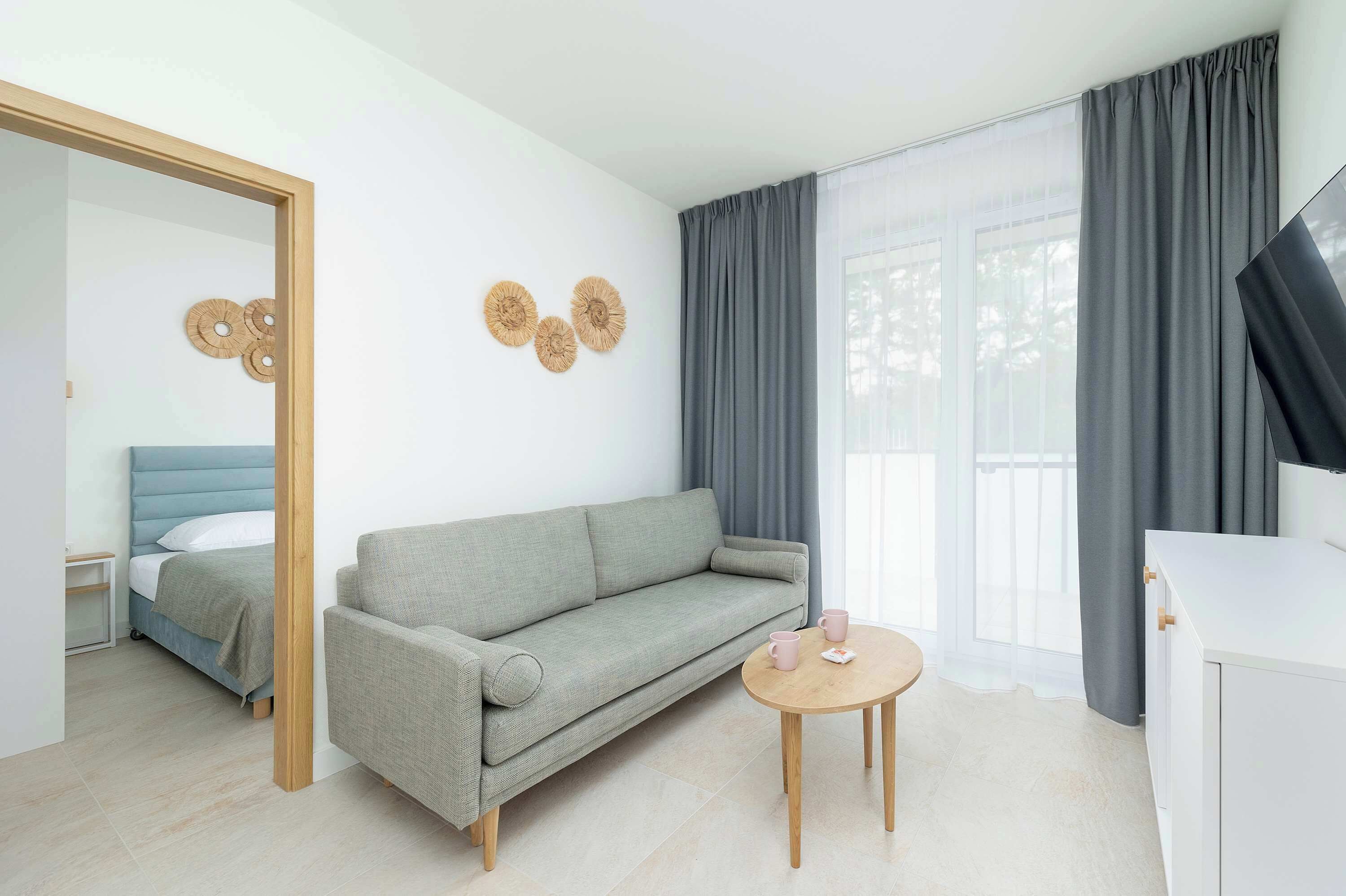 A modern room with a sofa, a small round table, a bed with a blue headboard, and a large mirror.