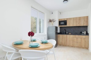 A modern kitchen with wooden cabinets, a microwave, and a sink. There is a dining area with a round table and white chairs.