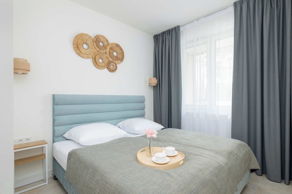The apartment’s bedroom is decorated in neutral tones with cozy bedding and decorative wall art, offering a calming ambiance. Large windows provide ample natural light, and the room is equipped with essentials like bedside tables and reading lamps.