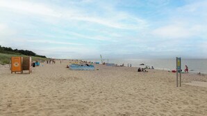 A beach with sand, a few umbrellas, and a sign. - Cozy Apartment close to the beach | Parking in the garage (Dąbki)