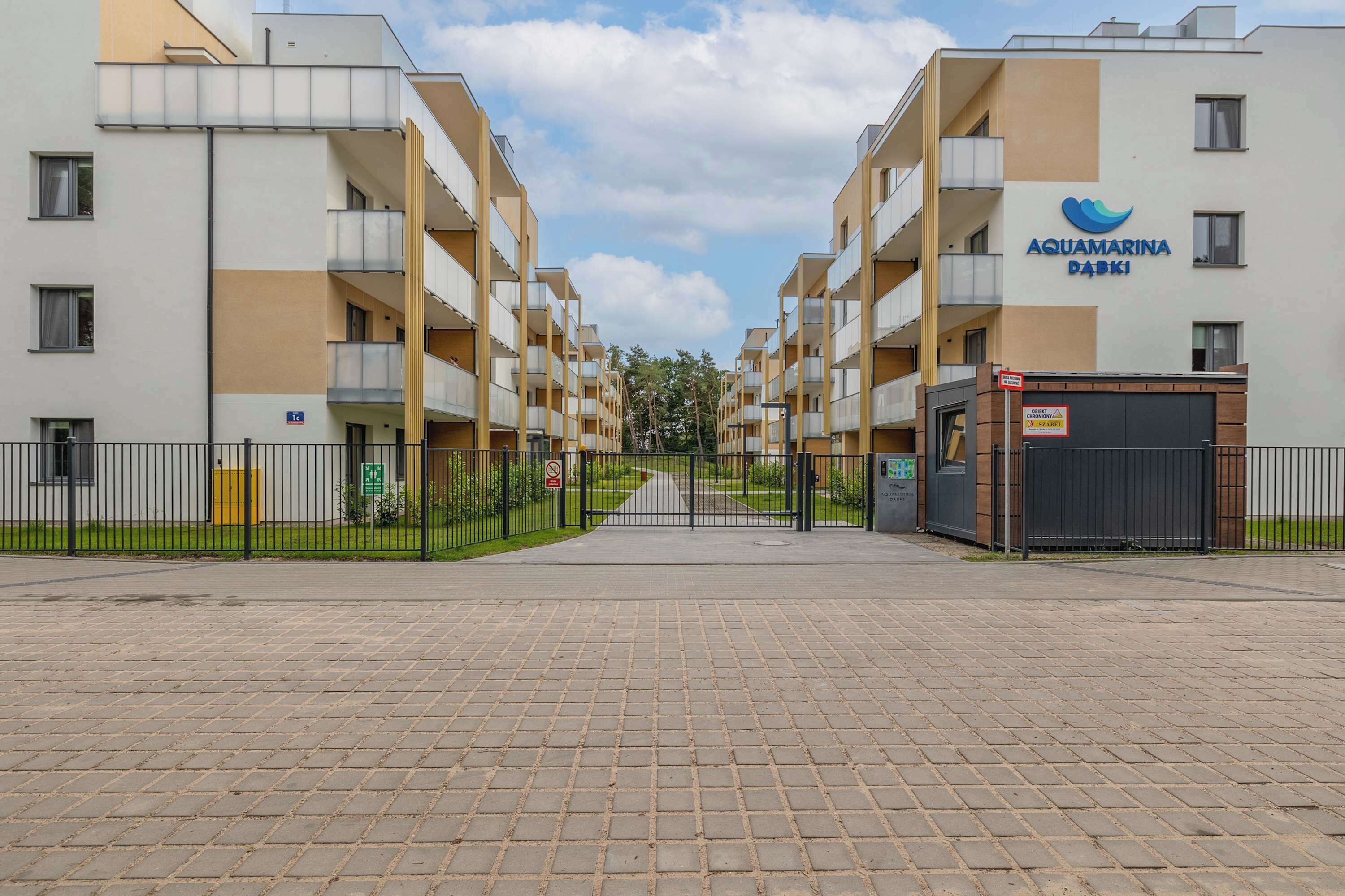 A modern apartment building with a gated entrance, multiple balconies, and a clear sky.