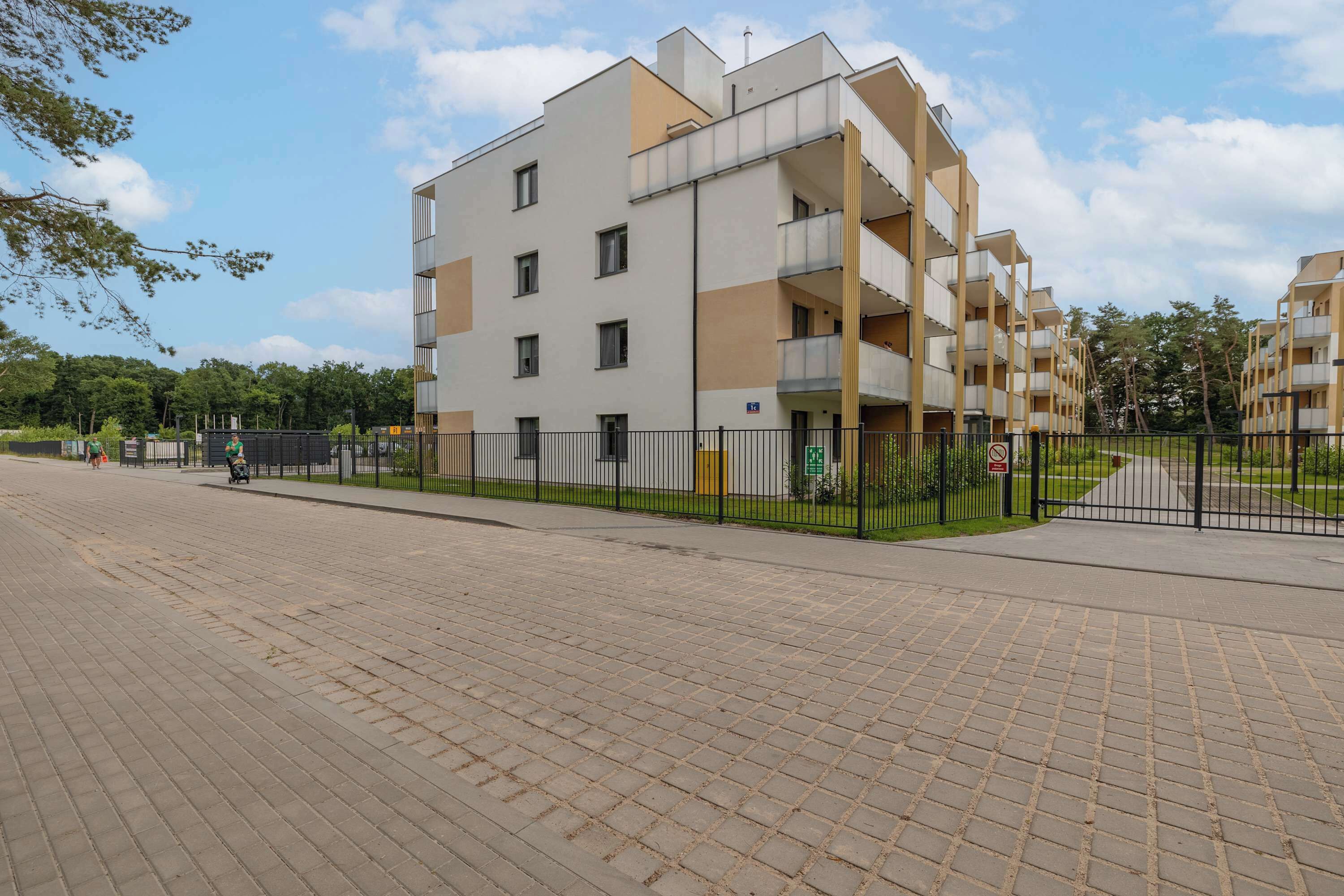 Un edificio residencial de varios pisos con balcones, un sendero pavimentado y un área cercada.