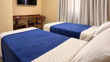 A hotel room with two beds, a desk, a chair, a television, and an air conditioning unit.