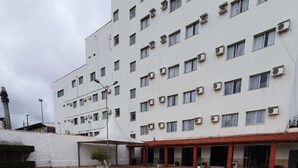 A swimming pool with a tiled deck, surrounded by a white building with multiple windows and air conditioning units. - Hotel Transcontinental (Ji Parana)