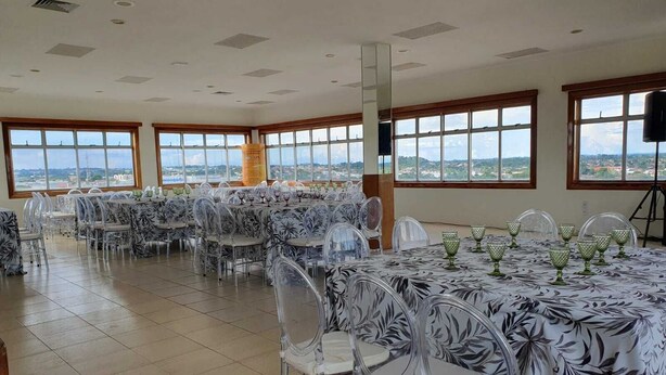 A spacious room with multiple tables and chairs, large windows offering a view of the city, and a high ceiling with recessed lighting. - Hotel Transcontinental (Ji Parana)