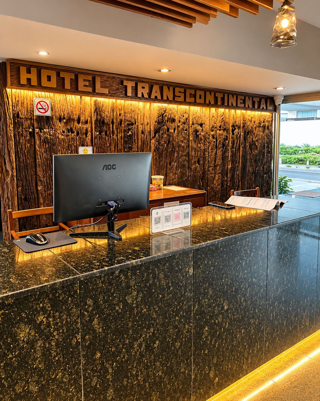 A hotel reception desk with a large monitor, a computer mouse, and a menu stand.