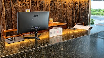 A hotel reception desk with a large monitor, a computer mouse, and a menu stand.