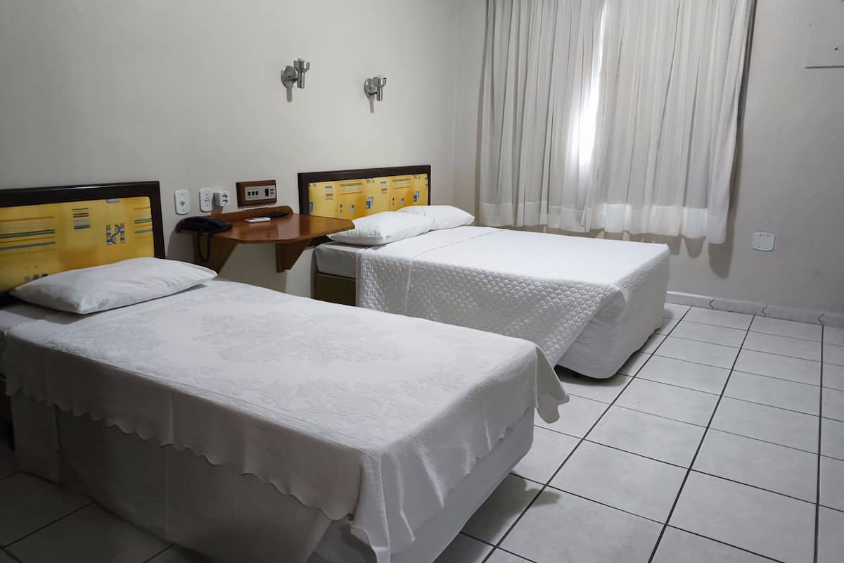 A hotel room with two single beds, a wooden nightstand, a telephone, and a window with white curtains.