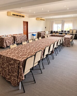 Une salle de conférence équipée de plusieurs tables et chaises, de climatiseurs et d’une porte.