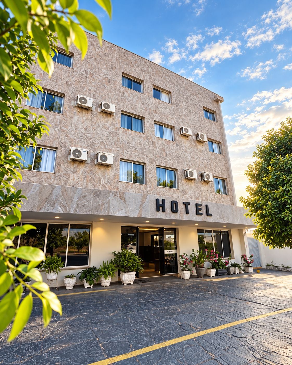 Un hotel con fachada moderna, múltiples unidades de aire acondicionado y una entrada acogedora con plantas en macetas.