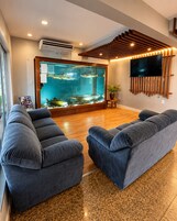 Una sala de estar moderna con un acuario grande, sofás grises, suelo de madera y un televisor montado en la pared.