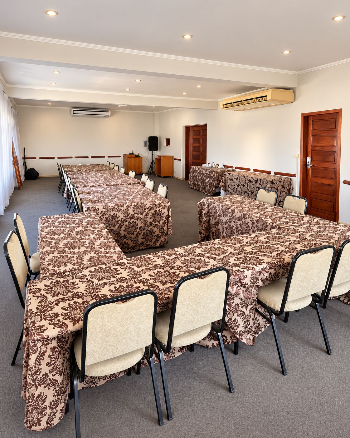 A conference room with a long table, chairs, an air conditioning unit, a speaker, and a door.