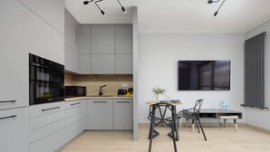 A modern kitchen with grey cabinets, a black oven, and a wooden countertop. There is a dining area with a table and chairs, and a potted plant on the table. - Comfortable Apartment in the Center | Parking, AC, Balcony (Warszawa)
