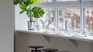 A window with a potted plant, three stools, and a table set with glasses and plates. - Modern Apartment | Air Conditioning | Close to Parks (Warszawa)