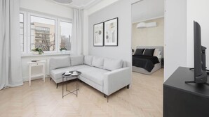 A modern living room with a grey sofa, a small side table, a large window with curtains, and a flat-screen TV on a black stand. - Modern Apartment | Air Conditioning | Close to Parks (Warszawa)