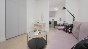 A modern living room with a round glass table, a pink sofa, and a white desk with a mirror. - Air-conditioned Studio in Warsaw | Close to Parks (Warszawa)