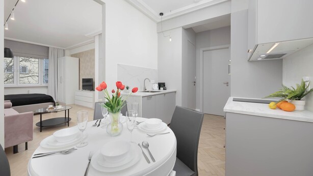 A modern, well-lit dining area with a round table set for four, a vase with red tulips, and a kitchen in the background. - Air-conditioned Studio in Warsaw | Close to Parks (Warszawa)