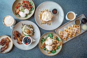 A breakfast spread with waffles, eggs, bacon, and various side dishes on a table.