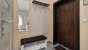 A hallway with a wooden door, a bench, a wall-mounted mirror, and a coat rack with hooks.