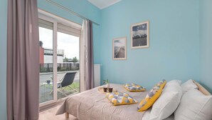 A bedroom with a large bed, a view through a sliding glass door, and two framed pictures on the wall.