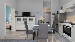A modern kitchen with a dining area, featuring a flat-screen TV, white cabinets, and a stainless steel refrigerator.