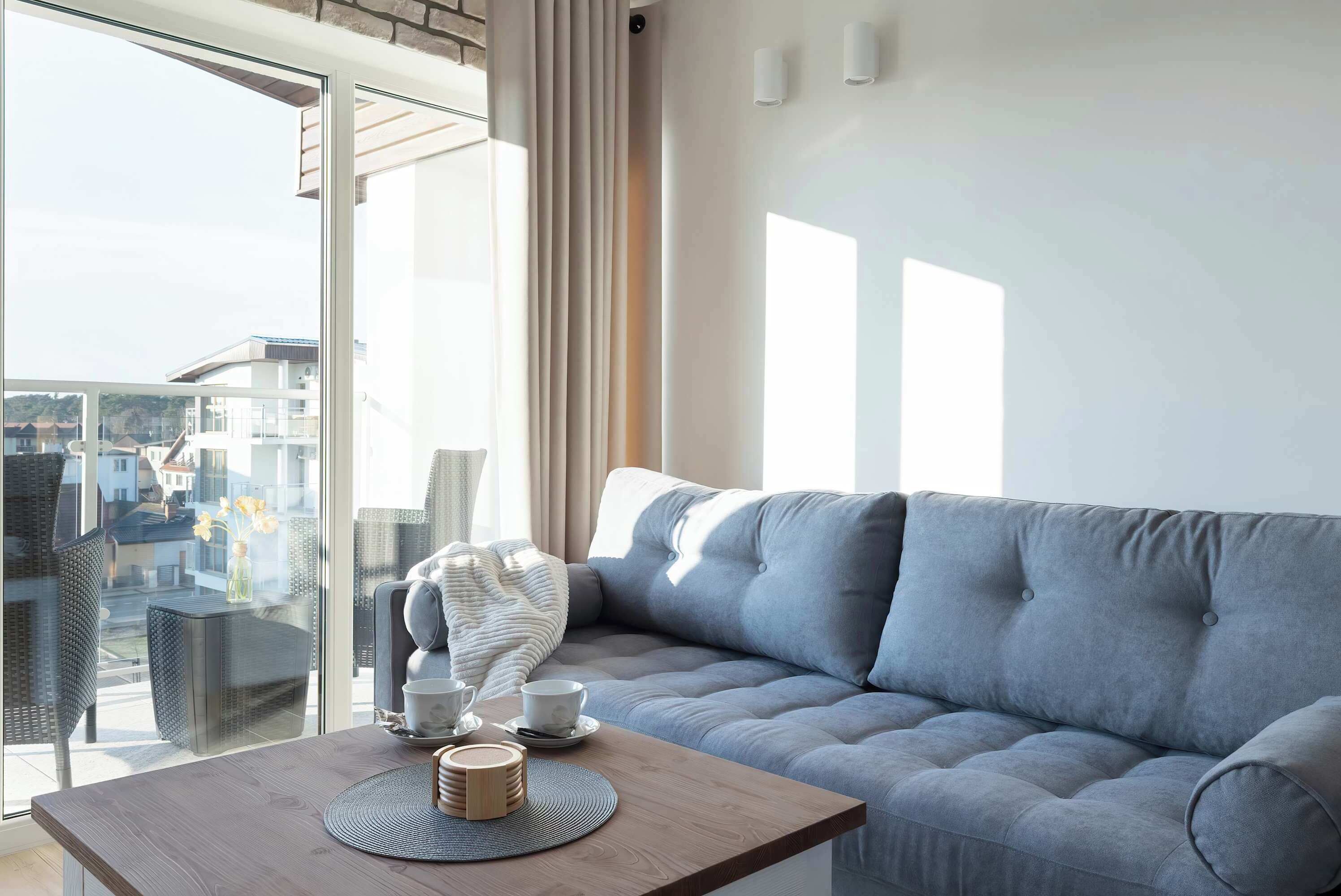 A modern living room with a grey sofa, a wooden coffee table, and a glass door leading to a balcony.