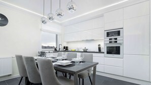 Una cocina moderna con armarios blancos, horno empotrado y comedor con mesa para cuatro.