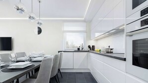 Una cocina moderna con armarios blancos, una mesa de comedor dispuesta con platos y vasos, y un ventanal que proporciona luz natural.