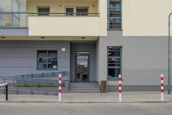 A modern building with a grey and yellow facade, a set of stairs leading to a door, and a metal railing on the left.