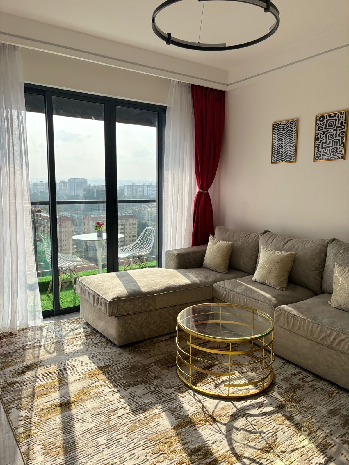 A modern living room with a sectional sofa, a glass coffee table, and a view of a cityscape through large windows.