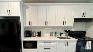A modern kitchen with white cabinets, a black refrigerator, a stove, and a microwave. - Spacious 2BR Retreat in Nature (Burk's Falls)