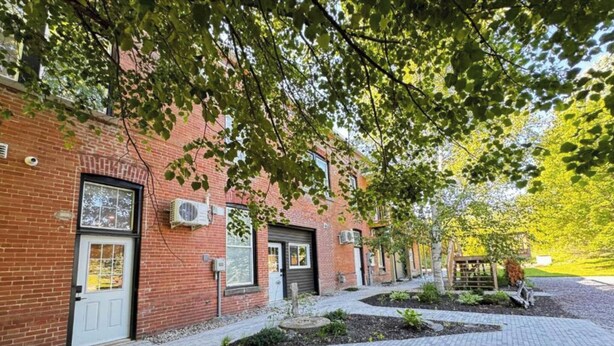 A brick building with a paved walkway and a small garden area. - Spacious 2BR Retreat in Nature (Burk's Falls)