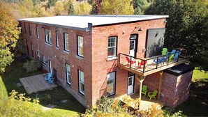 A two-story brick building with a flat roof, a balcony with colorful chairs, and a small deck area. - Spacious 2BR Retreat in Nature (Burk's Falls)