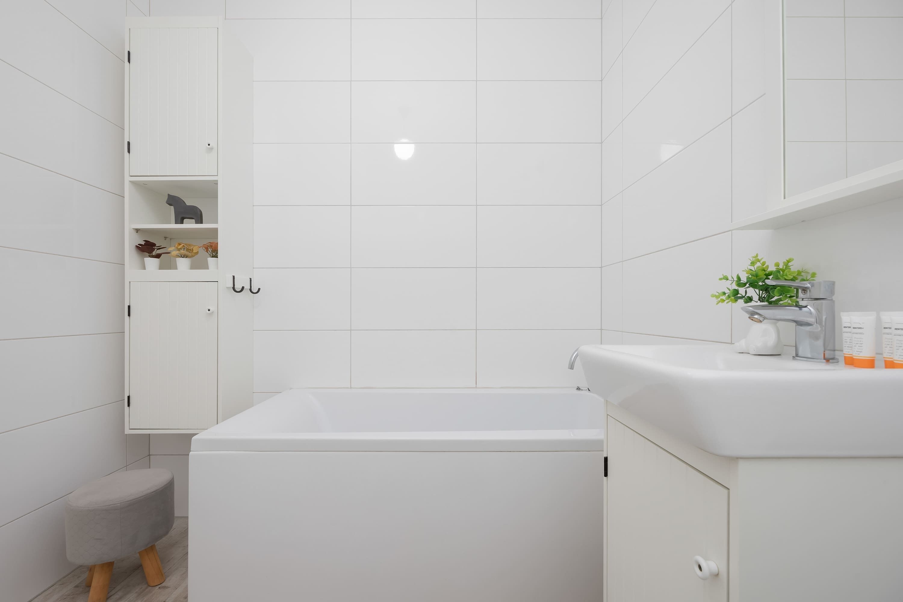 A modern bathroom with a white bathtub, a small stool, and a cabinet with toiletries.