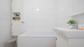 A modern bathroom with a white bathtub, a small stool, and a cabinet with toiletries.