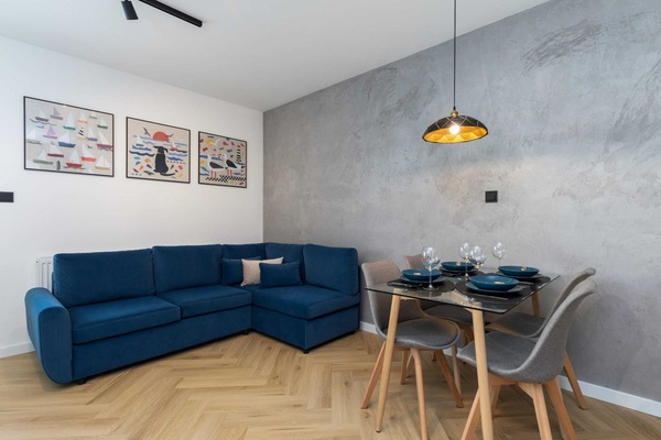 A stylish living and dining area featuring a blue corner sofa, a wooden dining table, and modern decor on the walls.